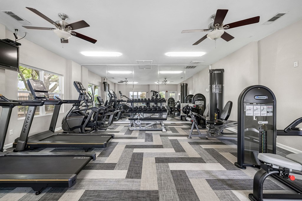 a gym with cardio machines and ceiling fans