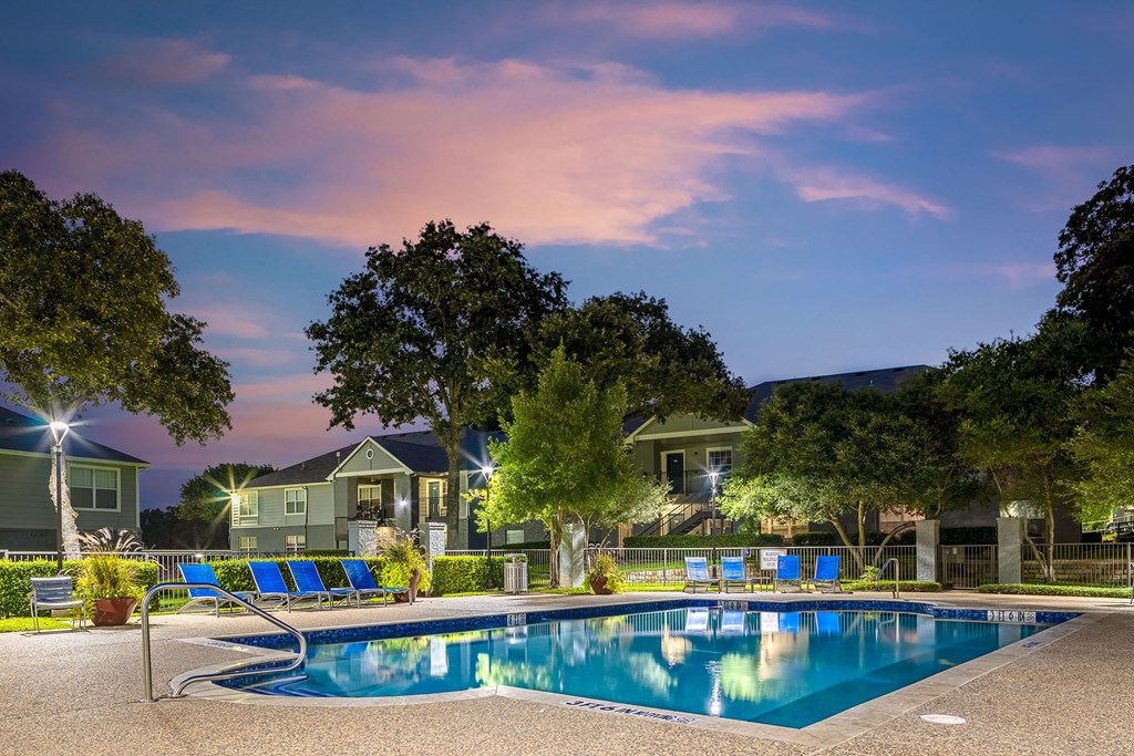 a swimming pool with blue chairs around it at night