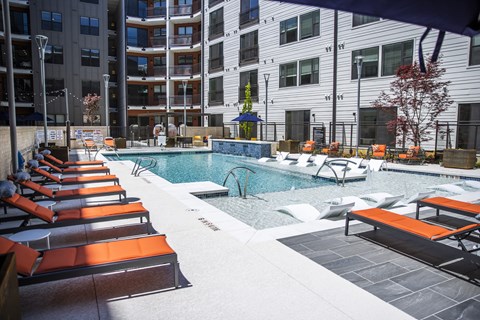 A pool area with sun loungers and a building in the background.