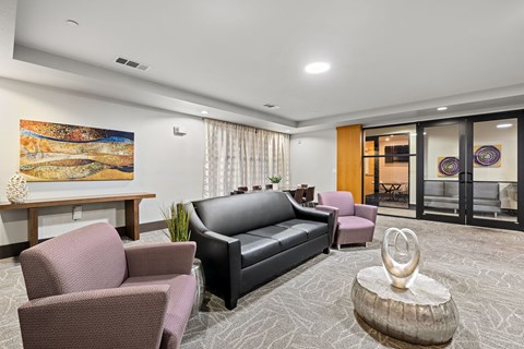 A living room with a grey carpet and a painting on the wall.