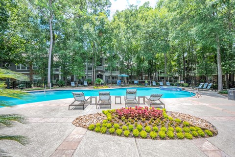 A pool surrounded by trees and chairs.