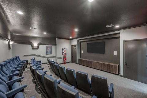 A row of blue seats are arranged in a dark room with a screen at the front.