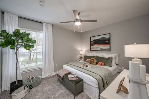 A bedroom with a bed, nightstand, and a plant.