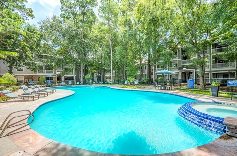 A large outdoor swimming pool surrounded by trees and lounge chairs.