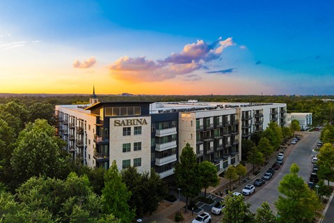 The image shows a large building with the name "SABINA" on it, surrounded by trees and parked cars.