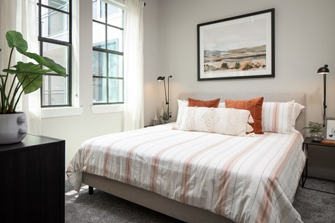 A bedroom with a bed, two lamps, and a painting on the wall.