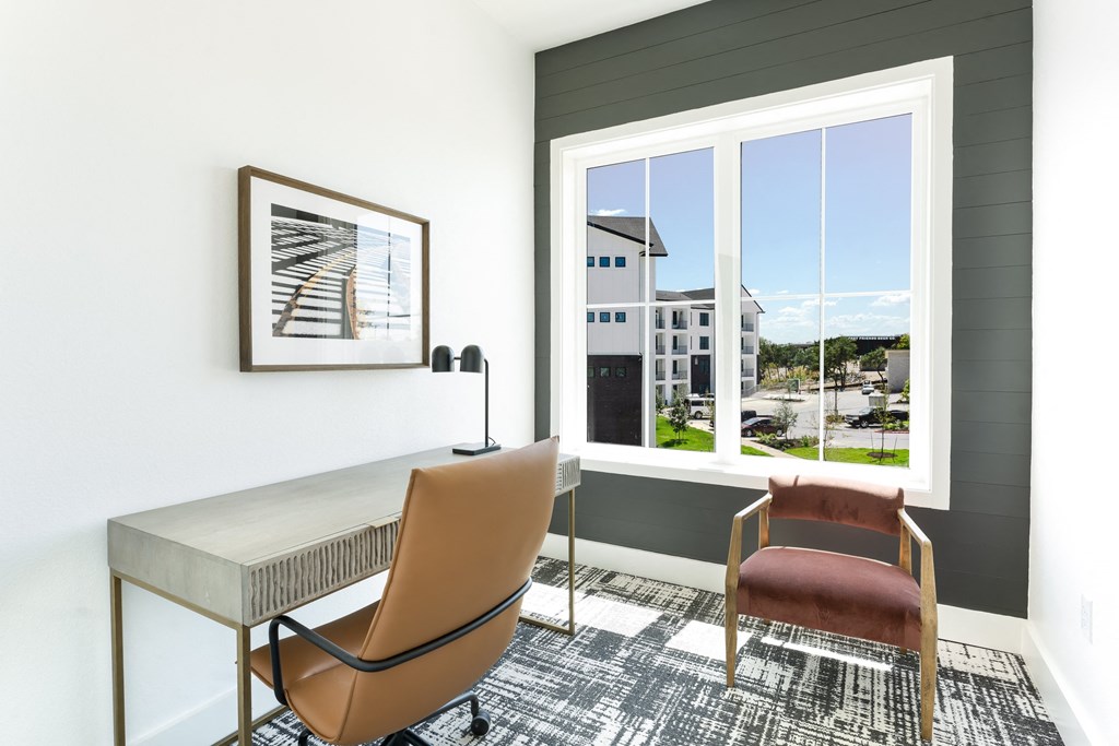 a room with a desk and two chairs and a large window