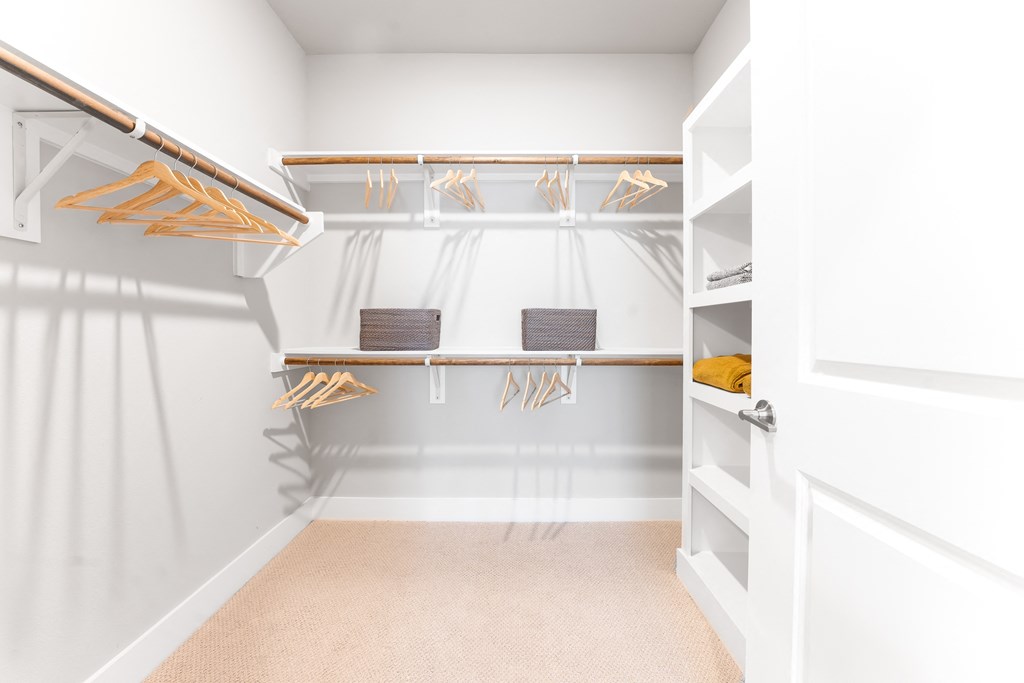 a walk in closet with white walls and shelves and a white closet door