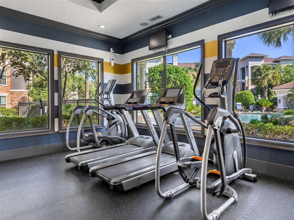 a gym with cardio equipment and large windows