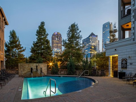 A pool surrounded by a stone wall with a city skyline in the background.