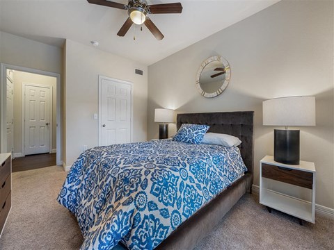 A bedroom with a bed, a ceiling fan, and a mirror on the wall.