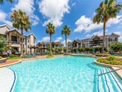 A swimming pool surrounded by palm trees and residential buildings.