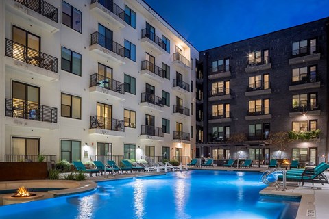 A swimming pool in front of apartment buildings at dusk.