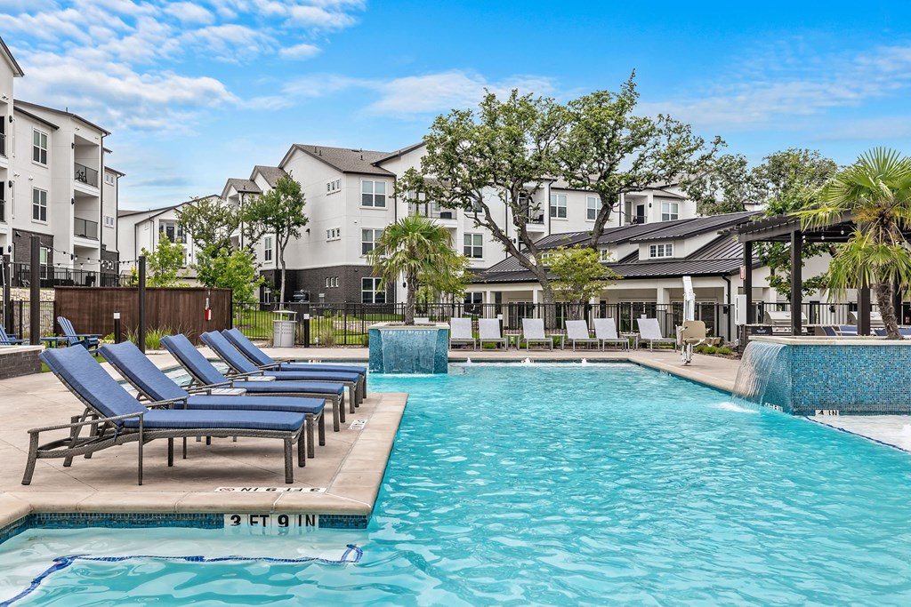 a swimming pool with blue lounge chairs next to an apartment building