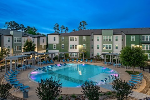 A swimming pool surrounded by lounge chairs and trees in front of apartment buildings.