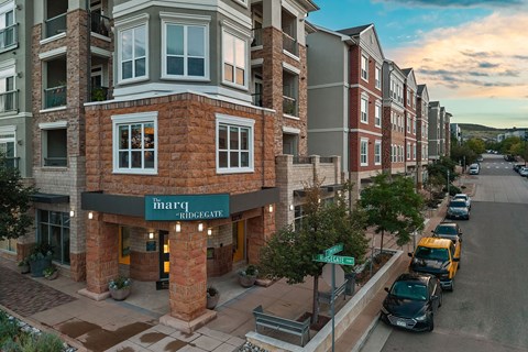 A street view of a row of apartment buildings with cars parked on the street.