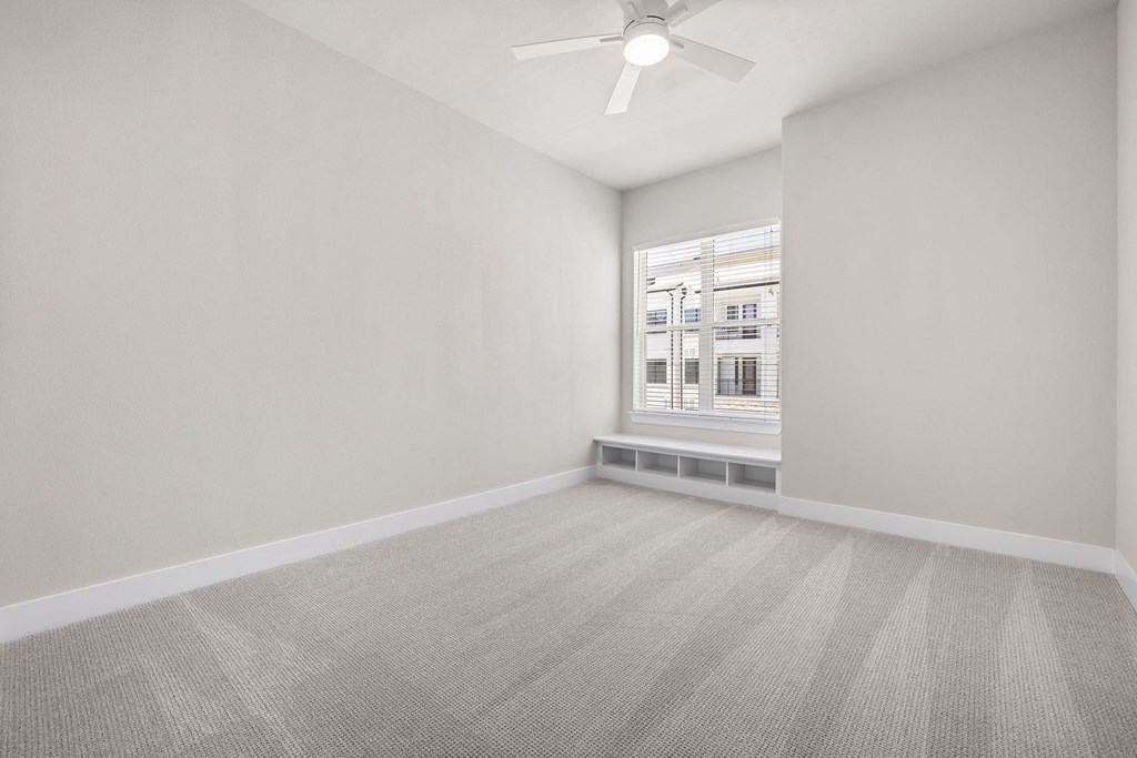 an empty living room with a window and a ceiling fan