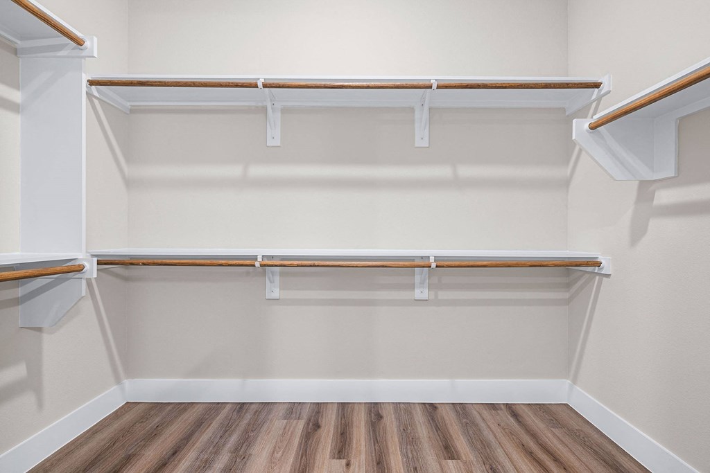 a walk in closet with shelves and a wooden floor
