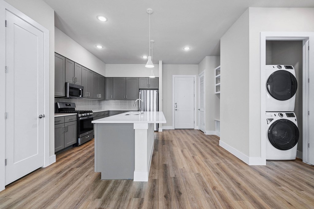 a living room with a washing machine and a kitchen with a sink