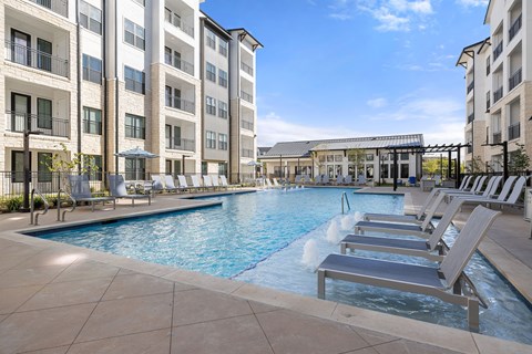 A large swimming pool with lounge chairs and a building in the background.