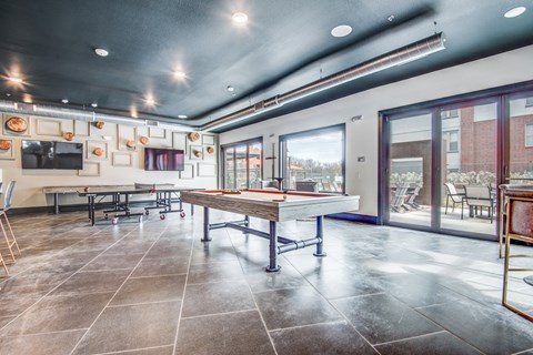 A room with a long table and chairs, a television, and a view of the outside through the windows.