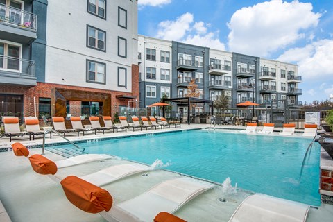 A swimming pool with orange chairs and a fountain in the middle.