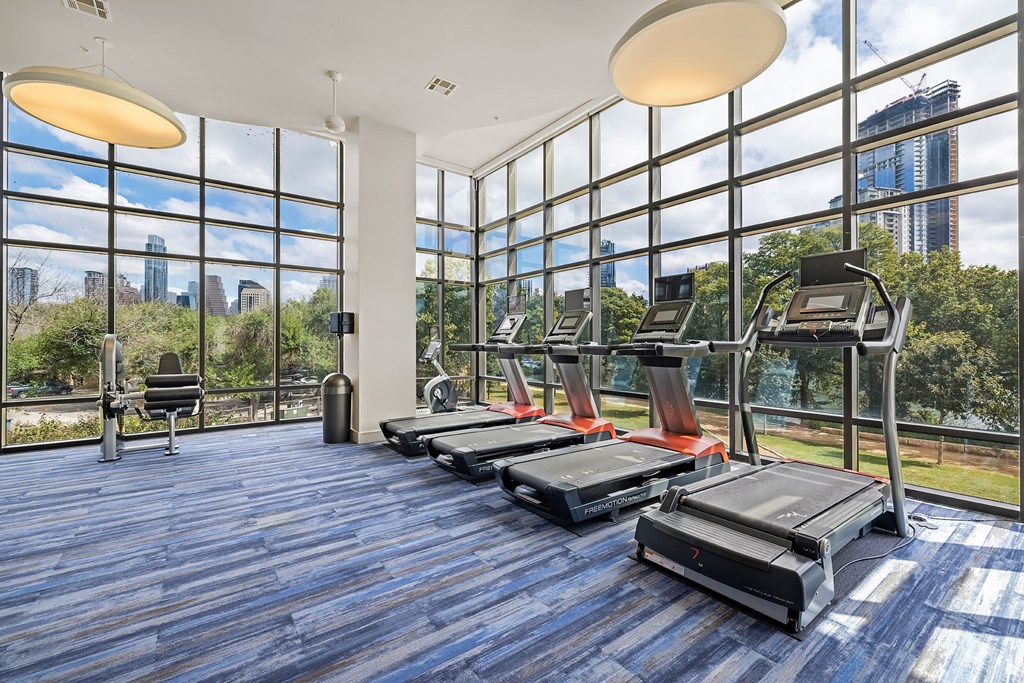 a gym with cardio machines and windows with a view of the city