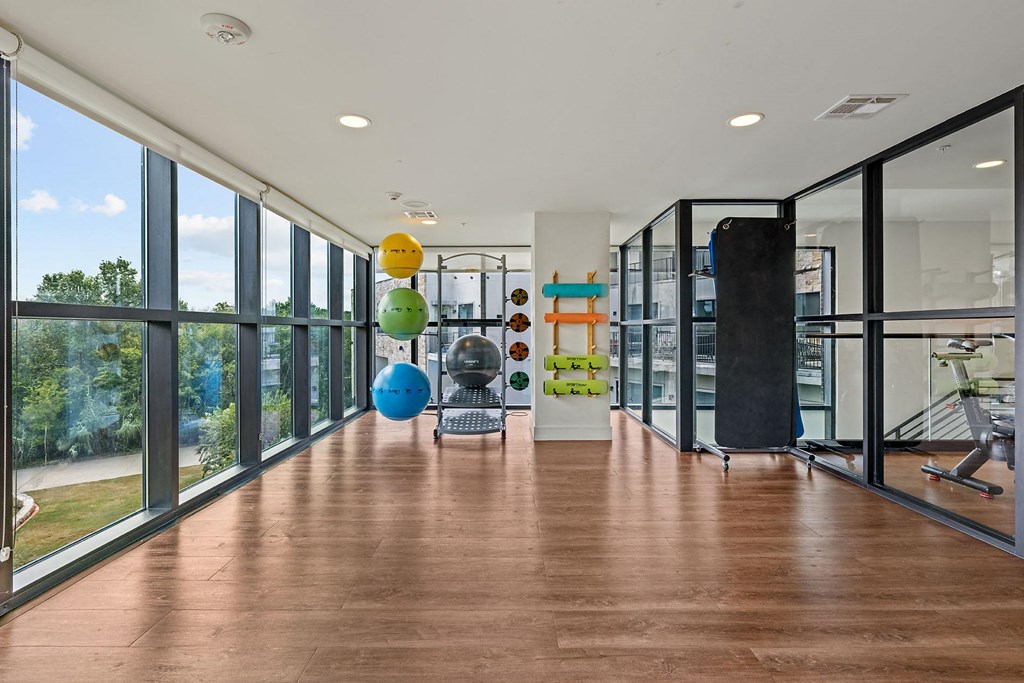 a gym with floor to ceiling windows and a wooden floor with weights and balls on