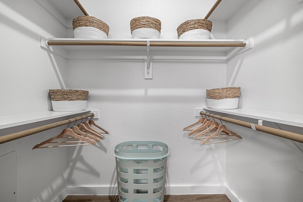 a walk in closet with baskets and hangers and a trash can