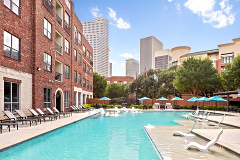 A pool surrounded by chairs and umbrellas in front of a brick building.