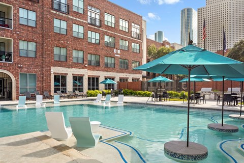 A pool with a blue umbrella and white chairs.