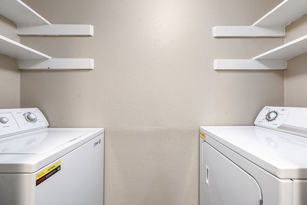 two washers and two dryers in a laundry room with shelves