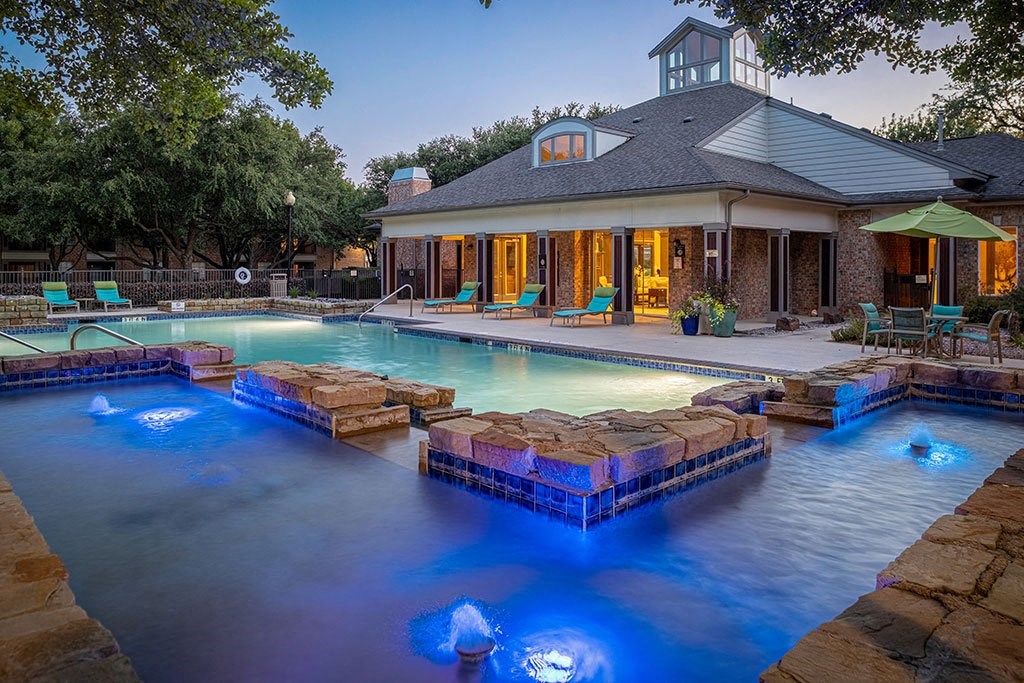 the pool is lit up at night in front of a house