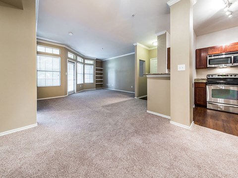 an empty living room with a kitchen with a stove and a microwave
