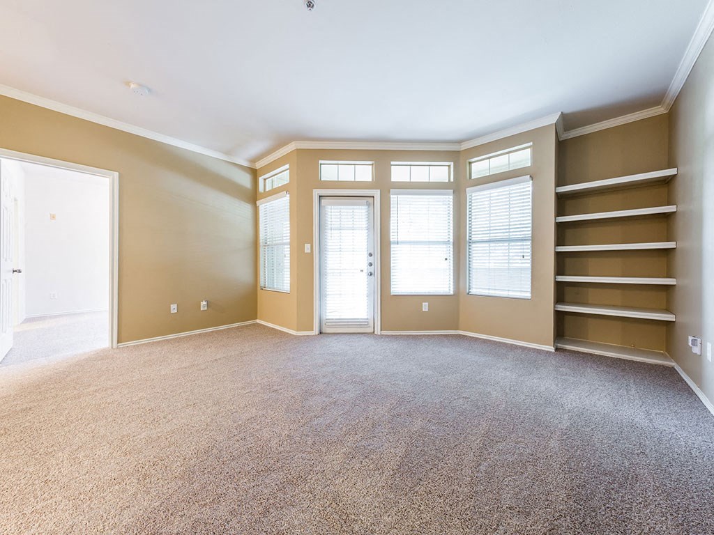 an empty living room with brown carpet and shelves
