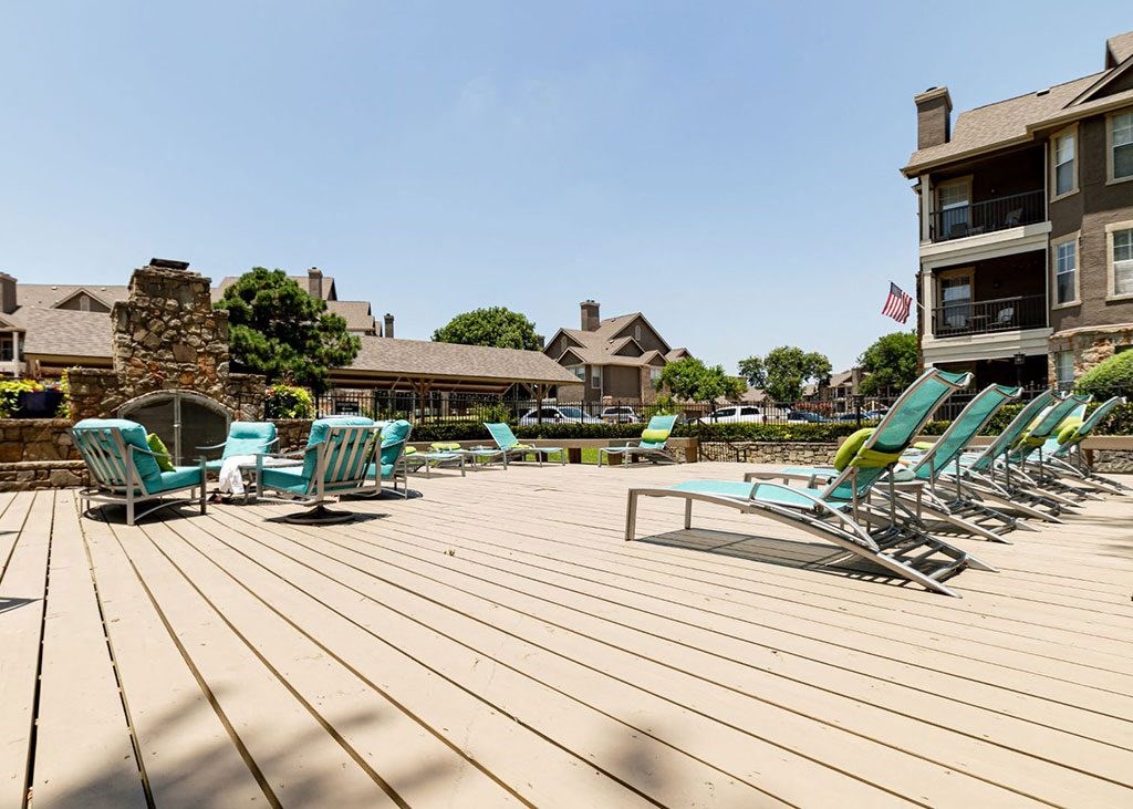 a large deck with chairs and a pool with a house in the background