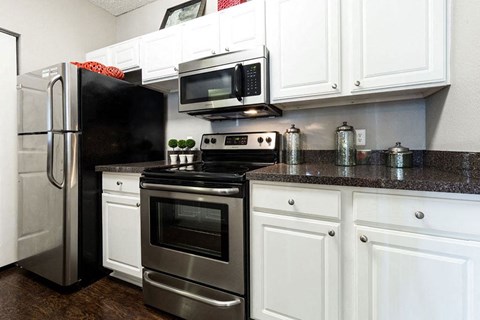 A black refrigerator is in a kitchen with white cabinets.