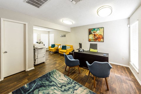 A room with a desk, chairs and a painting on the wall.