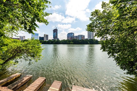 A serene lake with wooden docks and lush green trees in the foreground, with a city skyline in the background.