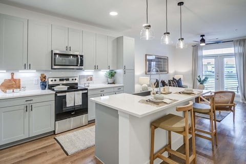 A modern kitchen with a white island and wooden chairs.