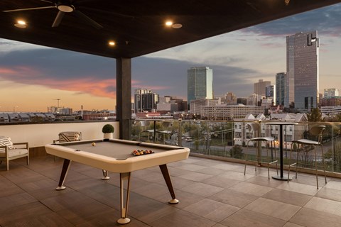 A pool table is on a balcony with a city skyline in the background.