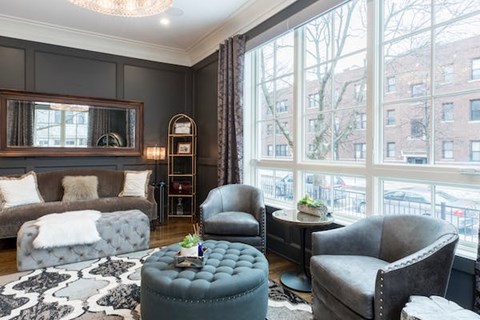 A living room with a grey ottoman, grey armchair, and a grey couch with a white throw.
