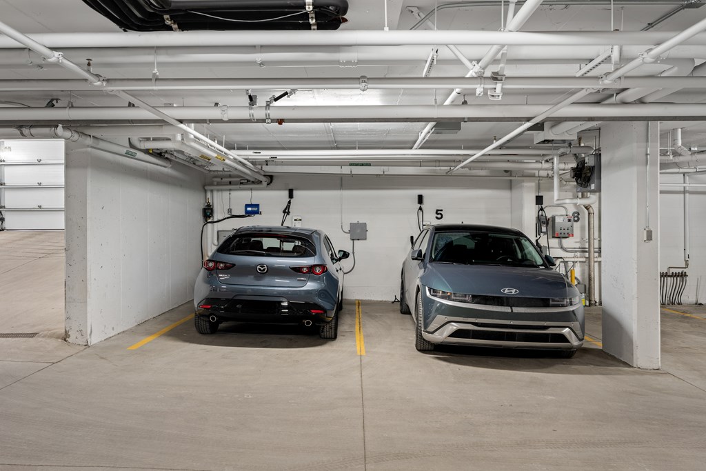 Two cars are parked in a garage with a white wall and a yellow line.