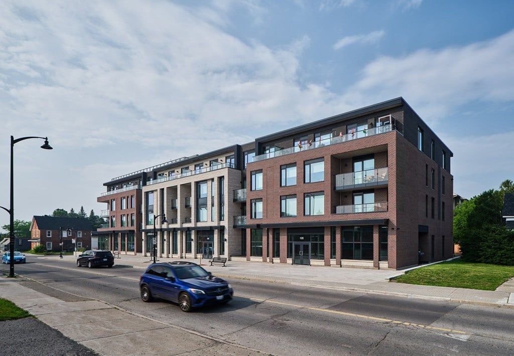 A blue car is driving on a road in front of a large building.