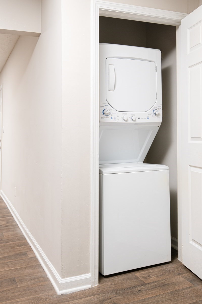 A white washing machine is in a small space between a wall and a door.