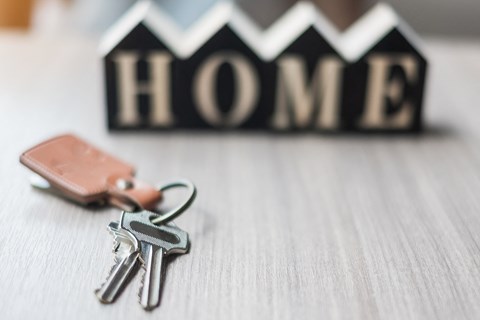 A set of keys and a wallet are placed in front of a HOME sign.