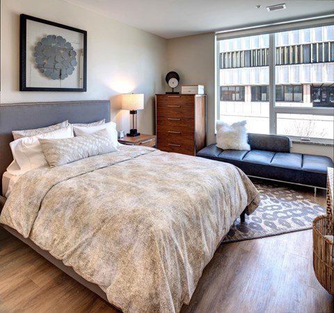 Downtown Kalamazoo Luxury Apartments - Spacious Bedroom With Wood-Inspired Plank Flooring, High Ceilings, And An Expansive Window With Views Of The Downtown Area