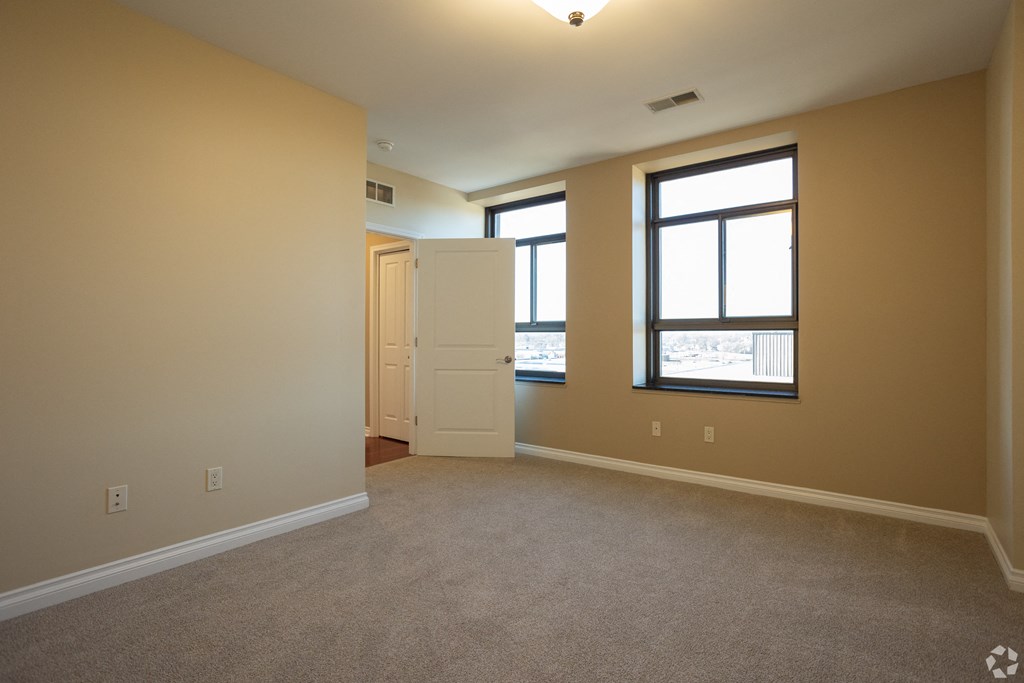 an empty living room with a door and two windows