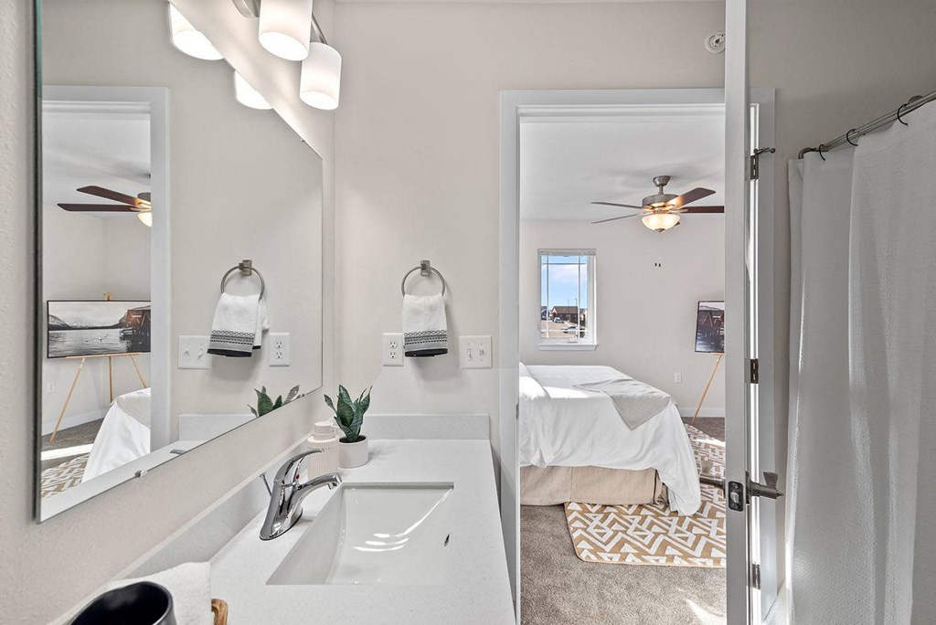 a bathroom with two sinks and a mirror and a room with a bed at The Residences Apartments at Bear Tree, DeForest, WI