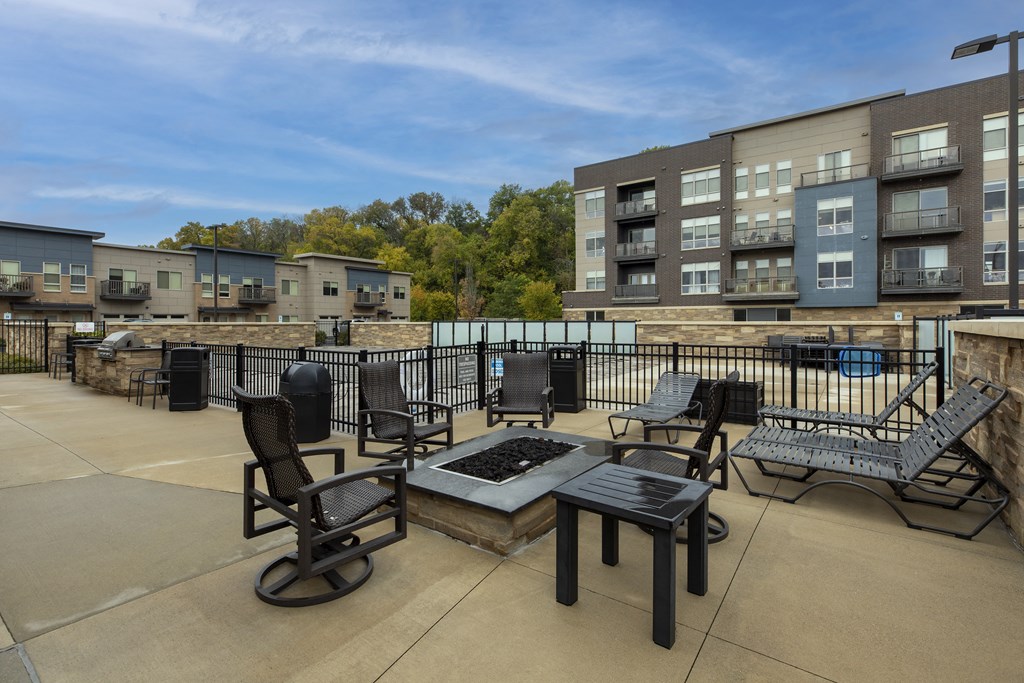 a patio with tables and chairs and a fire pit in front of an apartment building